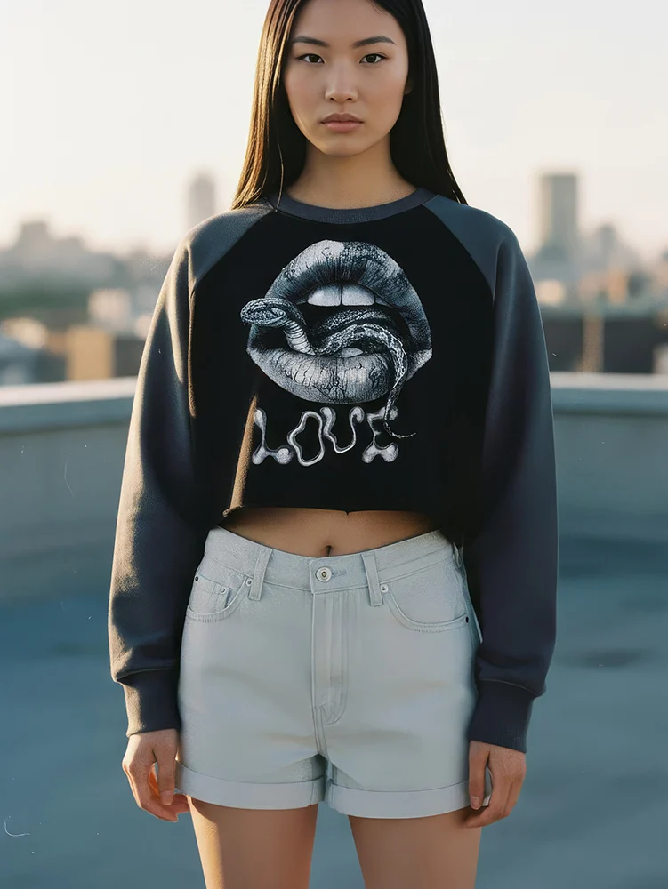 Unisex cropped crewneck sweatshirt with a black body and contrasting grey raglan sleeves. This stylish pullover features a large, detailed graphic of a snake emerging from a pair of lips, with the word 'LOVE' dripping below in a stylized font. The modern, cropped fit makes it a perfect statement piece for a streetwear or alternative fashion look.